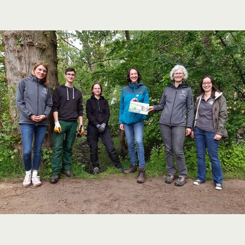Svenja Holst (3.v.r.) und Renate Schwarzmüller (2.v.r.) freuen sich über die gemeinsame Pflanzaktion. Ein Schild wird Besucher*innen auf den Standort der seltenen Einbeere hinweisen